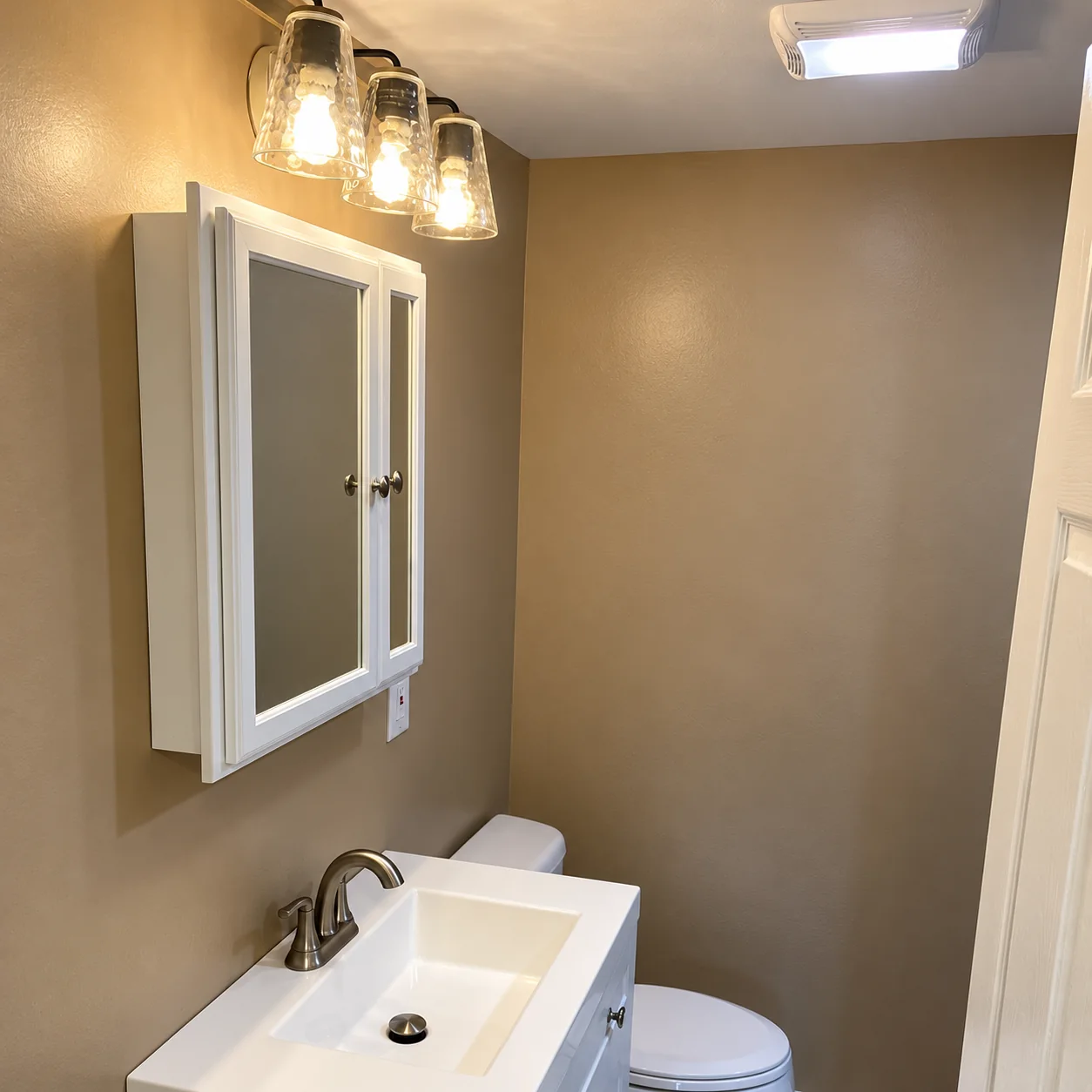 White bathroom vanity and mirrored cabinet with glass-shade lighting and warm beige walls