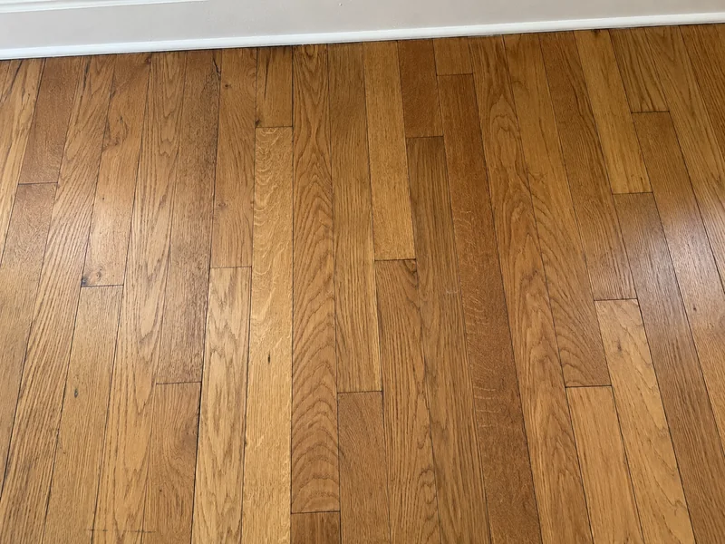 Warm oak floor strips with varied grain beside a white baseboard