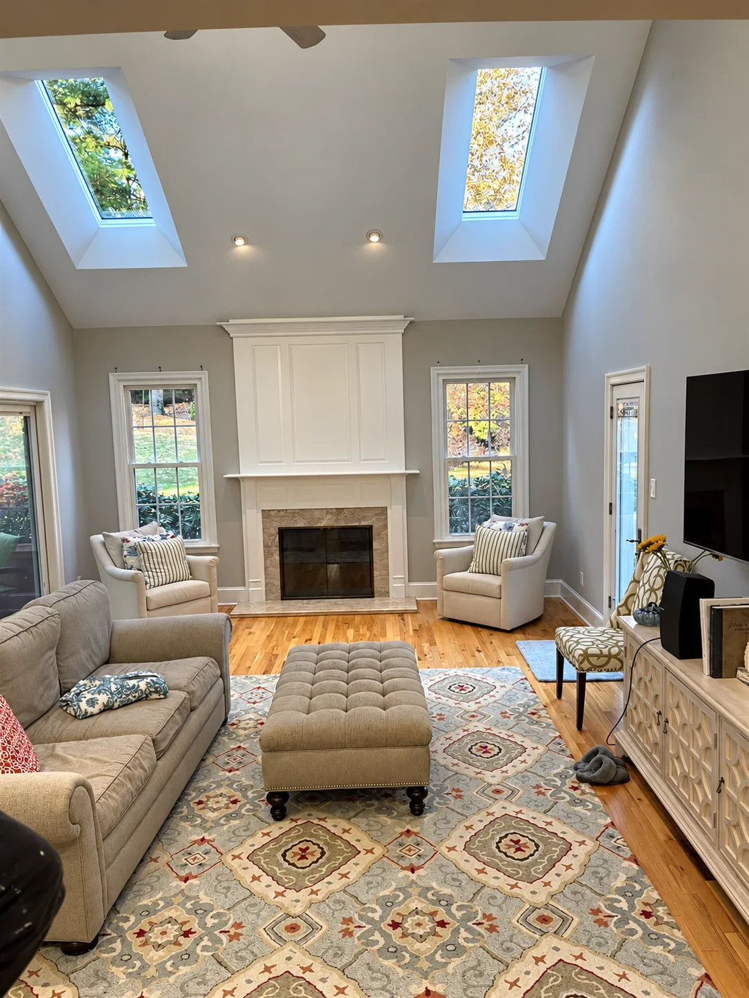 A light-filled living room with two skylights, a fireplace, timber flooring and detailed white trim